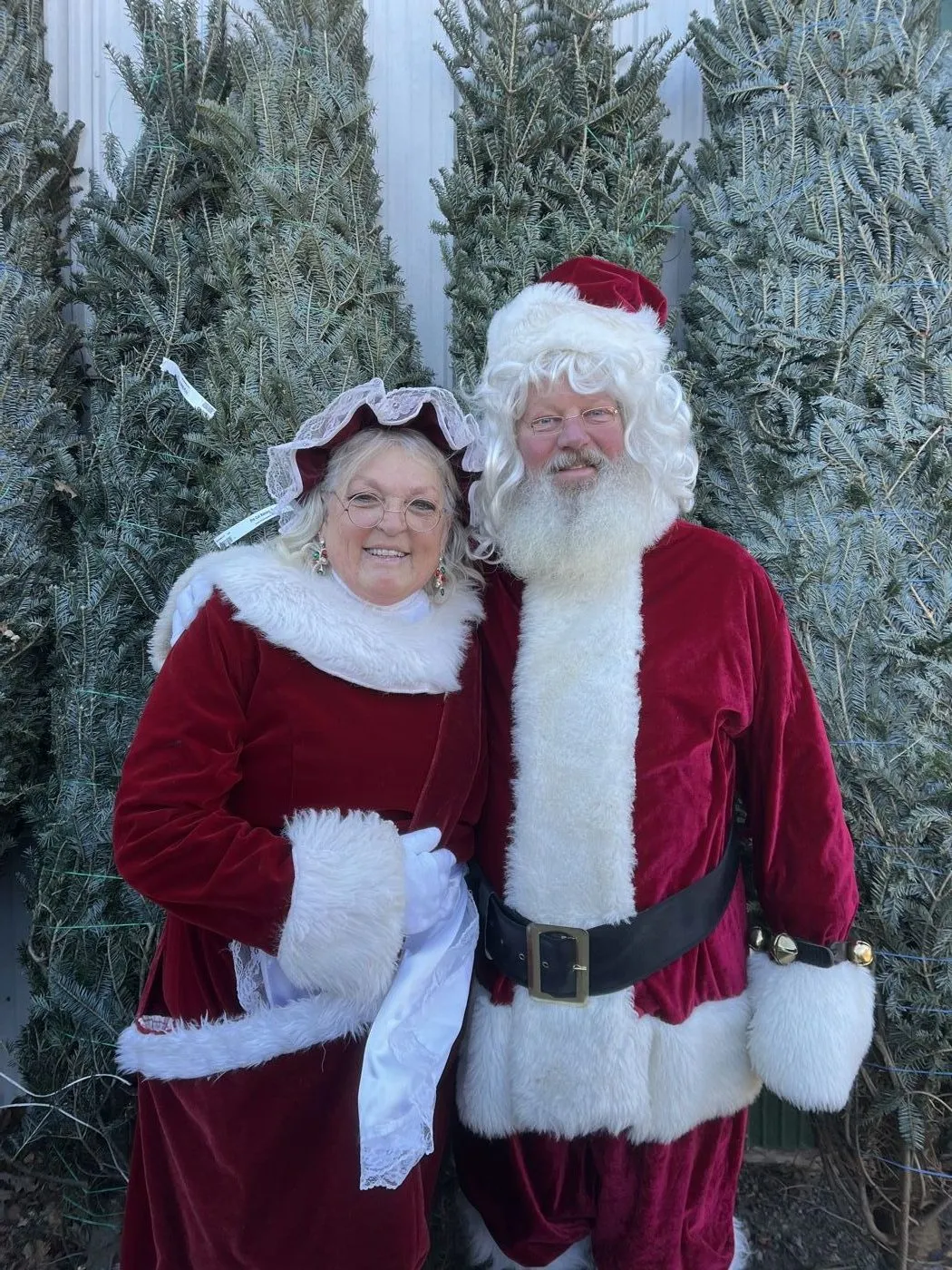 Santa and Mrs. Claus pose in front of Christmas trees at B&J Evergreen