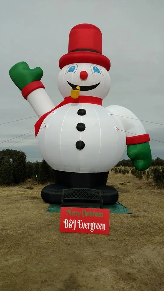 A giant inflatable snowman in a red top hat waving over the trees at the Princeton Tree Farm
